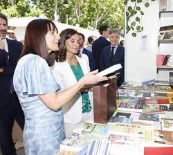 Durante el recorrido por la Feria del Libro, presentan varios libros a Su Majestad la Reina en el puesto de Andorra