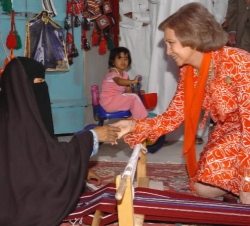 Doña Sofía saluda a una artesana mientras elabora una alfombra, durante su visita al Zoco Histórico